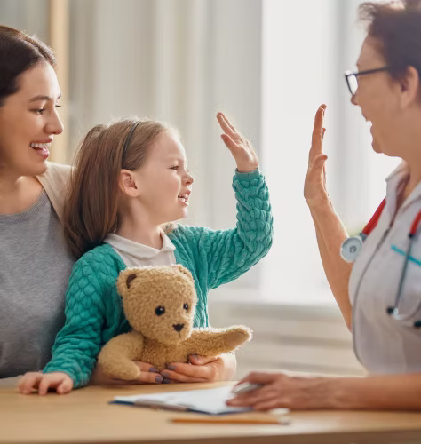 A smiling child high-fiving a doctor with a caregiver beside her